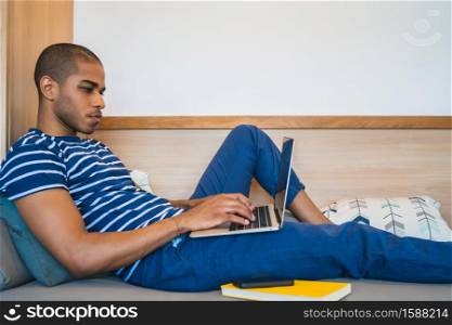 Portrait of young latin man lying on the sofa and using laptop at home. Lifestyle and technology concept.