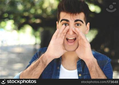 Portrait of young latin man shouting at camera. Outdoors