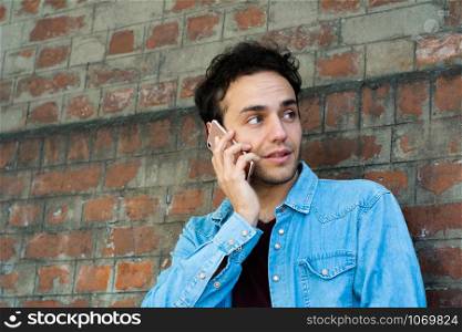 Portrait of young latin man talking on the phone against brick wall. Outdoors.