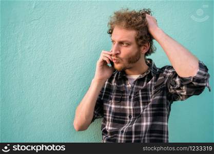 Portrait of young latin man talking on the phone against light blue background. Communication concept.
