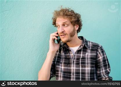 Portrait of young latin man talking on the phone against light blue background. Communication concept.