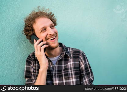 Portrait of young latin man talking on the phone against light blue background. Communication concept.