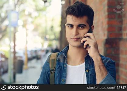 Portrait of young latin man talking on the phone in the street. Outdoors.