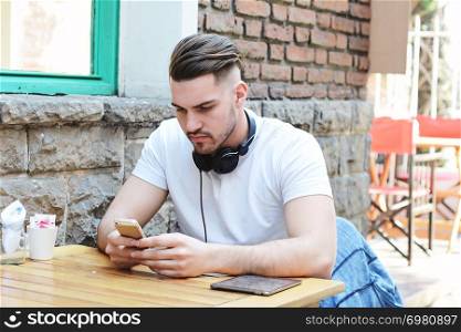 Portrait of young latin man typing on his phone. Outdoors.
