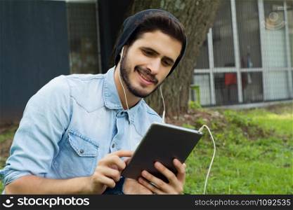 Portrait of young latin man using digital tablet in park . Outdoors.