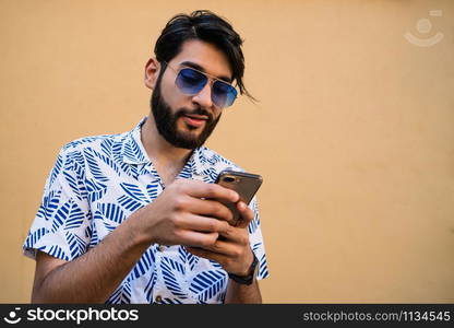 Portrait of young latin man using his mobile phone against yellow background. Communication concept.