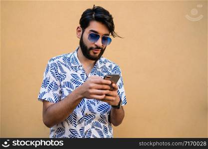 Portrait of young latin man using his mobile phone against yellow background. Communication concept.
