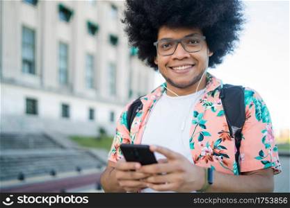 Portrait of young latin man using his mobile phone while standing outdoors on the street. Urban concept.