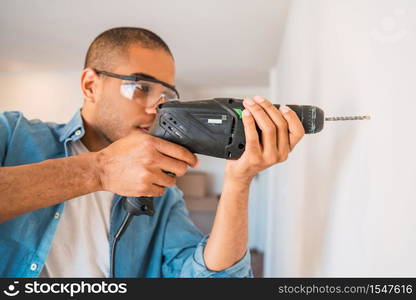 Portrait of young latin man with a electric drill and making hole in wall. Interior design and home renovation concept.