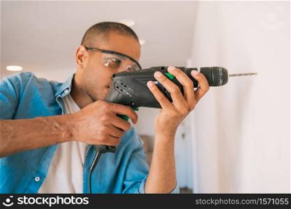 Portrait of young latin man with a electric drill and making hole in wall. Interior design and home renovation concept.