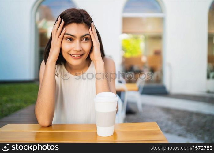 Portrait of young latin woman enjoying and drinking a cup of coffee outdoors at coffee shop. Lifestyle concept.