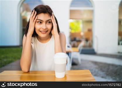 Portrait of young latin woman enjoying and drinking a cup of coffee outdoors at coffee shop. Lifestyle concept.