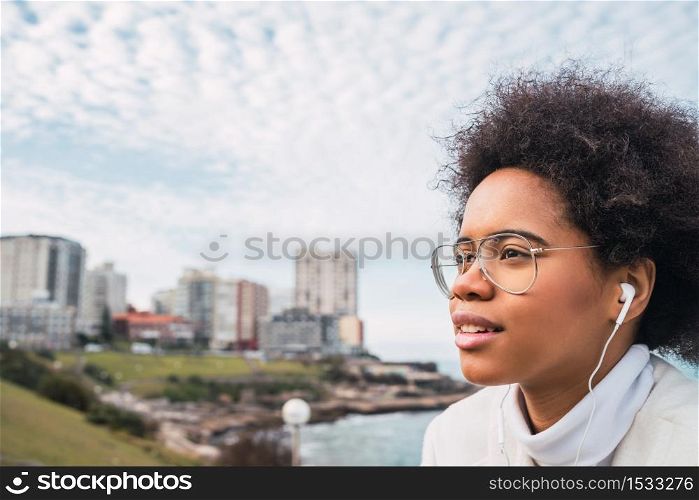Portrait of young latin woman enjoying free time and listening to music with earphones outdoors. Music, lifestyle.