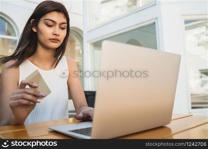 Portrait of young latin woman holding credit card and using laptop to shop online at a coffee shop. Shopping online and lifestyle concept.