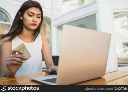 Portrait of young latin woman holding credit card and using laptop to shop online at a coffee shop. Shopping online and lifestyle concept.