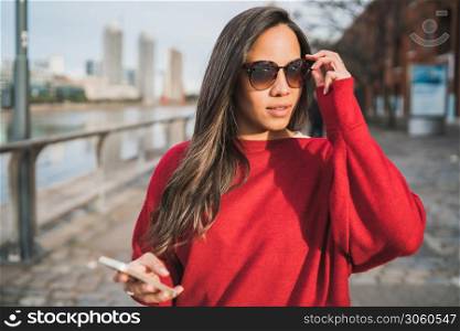 Portrait of young latin woman holding her mobile phone outdoors in the street. Urban concept.