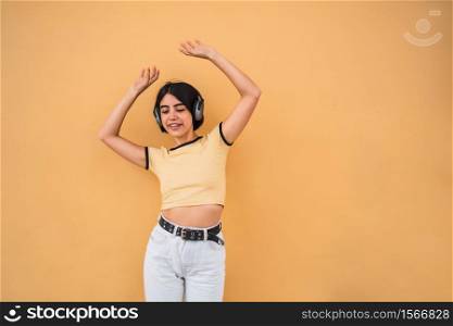 Portrait of young latin woman listening to music with headphones against yellow background. Urban concept.