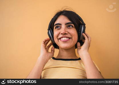 Portrait of young latin woman listening to music with headphones against yellow background. Urban concept.