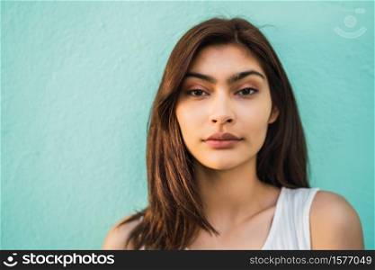 Portrait of young latin woman looking at camera on light blue background. Urban concept.