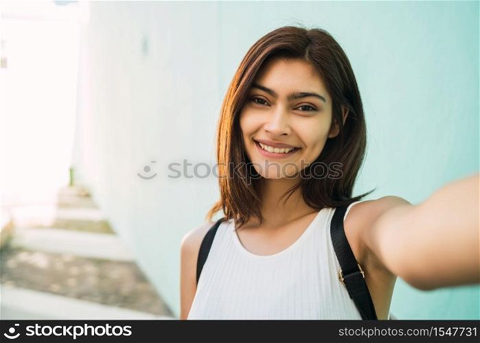 Portrait of young latin woman taking a selfie outdoors in the street. Lifestyle and urban concept.