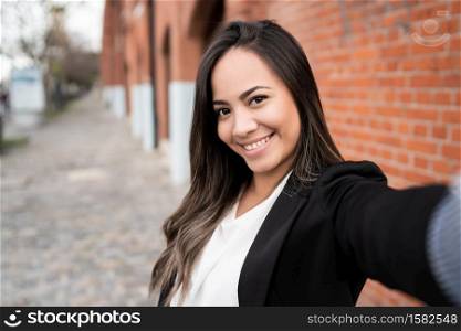 Portrait of young latin woman taking a selfie outdoors in the street.