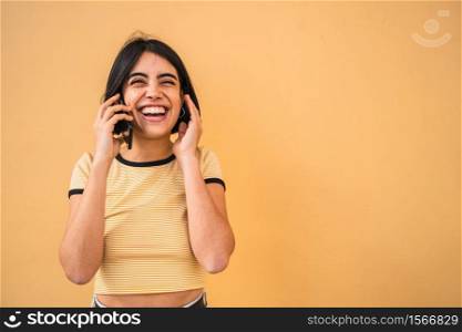 Portrait of young latin woman talking on the phone against yellow background. Communication and Urban concept.