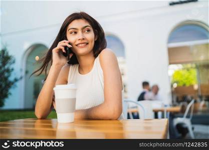 Portrait of young latin woman talking on the phone while sitting at coffee shop. Communication concept.