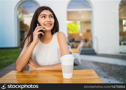 Portrait of young latin woman talking on the phone while sitting at coffee shop. Communication concept.