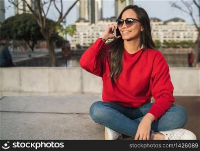 Portrait of young latin woman talking on the phone while sitting outdoors. Urban concept.