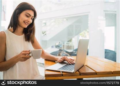 Portrait of young latin woman using her laptop while sitting in a coffee shop. Technology and lifestyle concept.