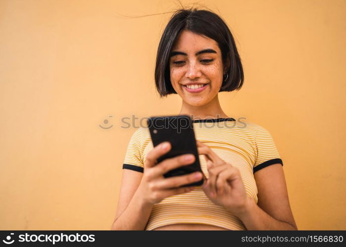 Portrait of young latin woman using her mobile phone outdoors in the street. Urban and communication concept.