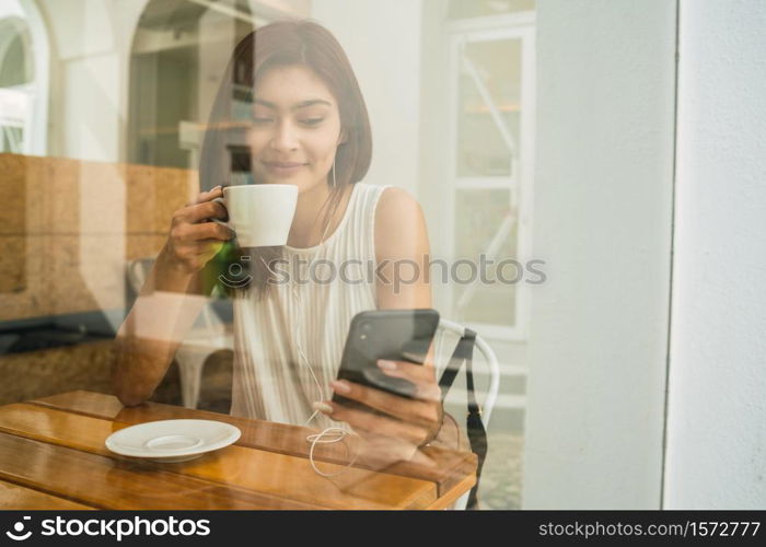 Portrait of young latin woman using her mobile phone while sitting at coffee shop. Communication concept.