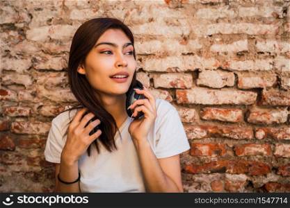Portrait of young latin woman with headphones against brick wall. Urban concept.