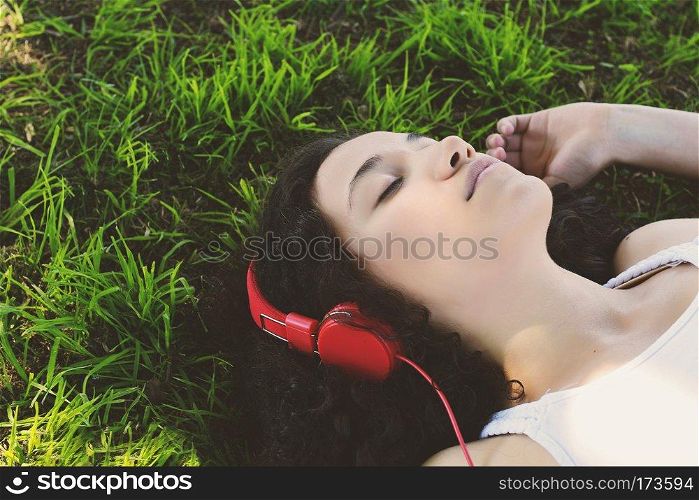 Portrait of young latin woman with headphones listening to music at the park in summer. Enjoying Music.