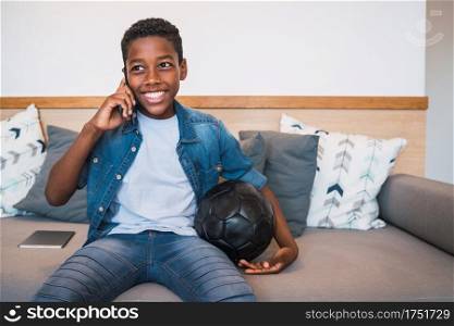 Portrait of young little boy talking on the phone with someone while sitting on couch at home. Communication concept.