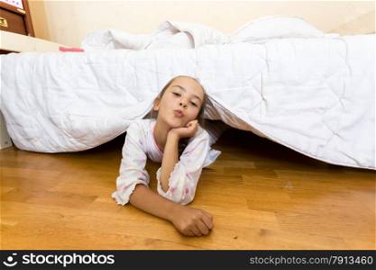 Portrait of young little girl lying on floor at bedroom under bed