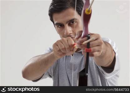 Portrait of young male archer practicing archery against gray background
