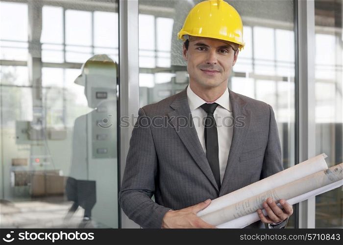 Portrait of young male architect holding rolled up blueprints in industry