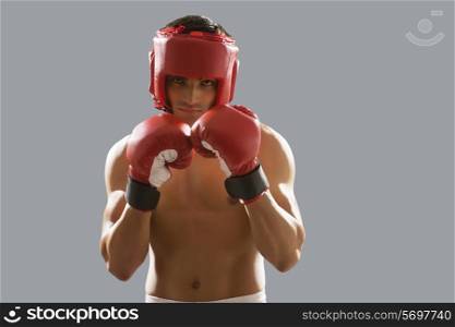 Portrait of young male boxer wearing gloves and head protector isolated over gray background