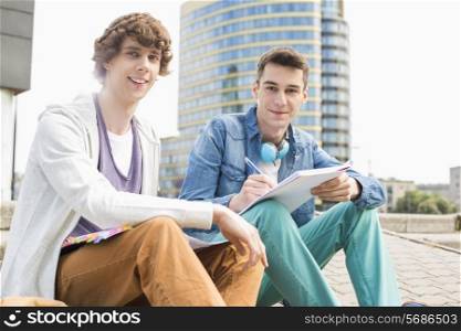 Portrait of young male college students studying on steps against building