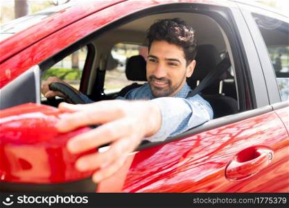 Portrait of young male driving his car and moving rear view wing mirror. Transport concept.