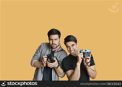 Portrait of young male friends with digital camera over colored background