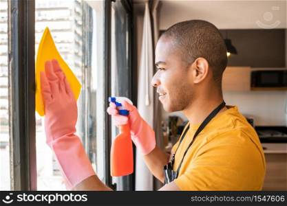 Portrait of young male housekeeper cleaning glass window at home. Housekeeping and cleaning concept.