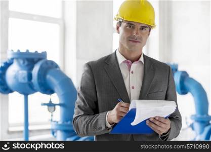 Portrait of young male manager writing on clipboard in industry