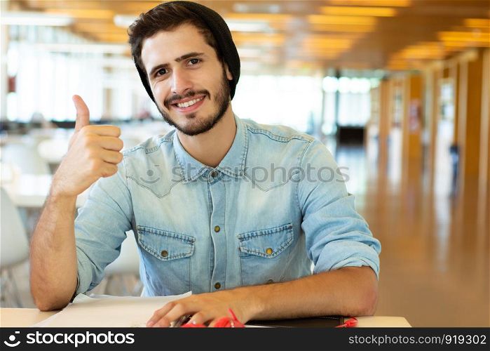 Portrait of Young male student showing thumbs up in the university library.