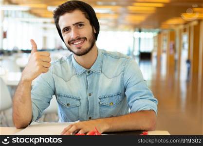 Portrait of Young male student showing thumbs up in the university library.