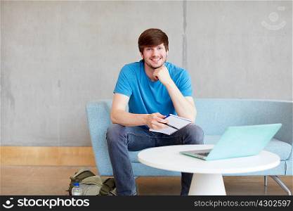 Portrait of young male student sitting on study space sofa at higher education college