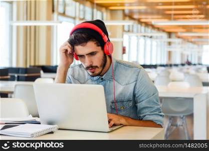 Portrait of young male student using laptop and learning online at the university library. Education and lifestyle concept.