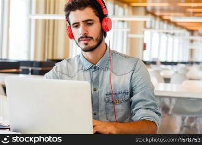 Portrait of young male student using laptop and learning online at the university library. Education and lifestyle concept.