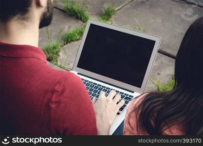 Portrait of Young male student using laptop and learning online outdoor.